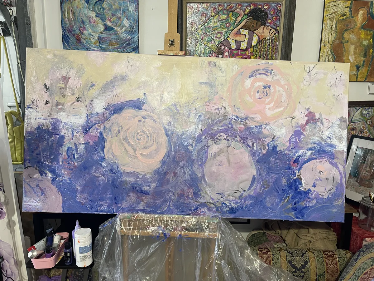 Early underpainting of the commission — loose blue, cream and blush layers with faint rose shapes, on the easel in Agata May'kowska's studio
