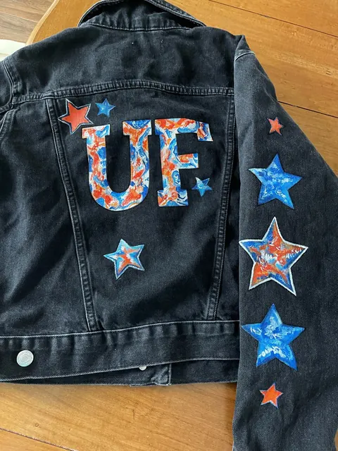 Sold original by Agata May'kowska — Black denim jacket with red, blue, and orange star patches and 'UE' spelled out with a colorful, abstract pattern on the back.
