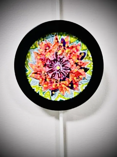 Sold original by Agata May'kowska — A colorful circular abstract artwork with a black border, featuring vibrant red, pink, orange, green, purple, and blue patterns, displayed on a white wall.